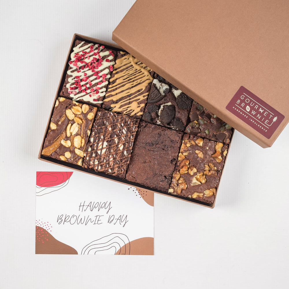 Chocolate brownies shown in a gift box.  All chocolate brownies with different toppings and chocolate drizzles.  Shows a 'Happy Brownie' day gift card.
