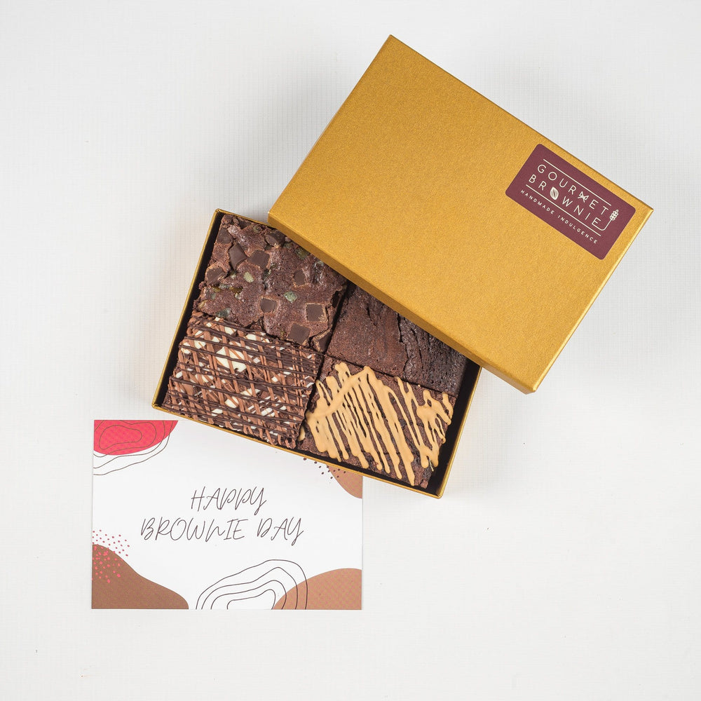 Small chocolate brownie gift box showing four slices of brownie.  Each a different flavour and topped with different ingredients or chocolate drizzle.  'Happy Brownie Day' gift card under box of brownies.