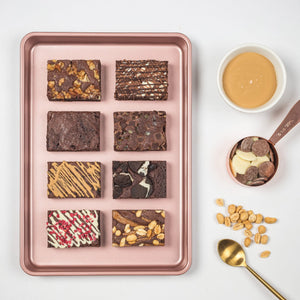 
                  
                    Load image into Gallery viewer, Eight slices of chocolate brownies shown in a baking pan. Each chocolate brownie has a different topping or chocolate drizzle. Next to baking pan are baking utensils and dishes holding chocolate.
                  
                